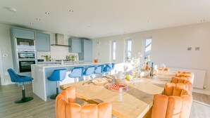 A modern kitchen with a central island, blue bar stools, and a dining area with orange chairs. - Garreg Hen -  a sea view that sleeps 8 guests  in 4 bedrooms (Trearddur Bay)