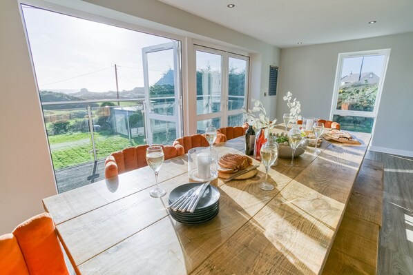 A dining area with a large table, orange chairs, and a view of a green landscape through large windows.