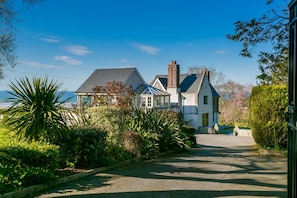 A two-story house with a driveway leading to the entrance, surrounded by lush greenery and a clear sky. - Gwynaeth Gwyn -  a hot tub that sleeps 16 guests  in 8 bedrooms (Wern y Wylan)