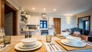 A modern kitchen with white cabinets, a stainless steel range hood, and a brick backsplash. There is a dining area with a wooden table set for two, featuring white plates, glasses, and cutlery.