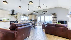 Une cuisine moderne avec des luminaires suspendus, un coin repas avec une table et des chaises, et un salon avec des canapés en cuir.
