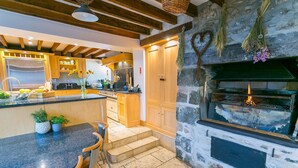 A kitchen with a stone wall, wooden beams, a stone fireplace, and a modern stove. - Tal y Bont Barns -  a remote that sleeps 24 guests  in 9 bedrooms (Bangor)