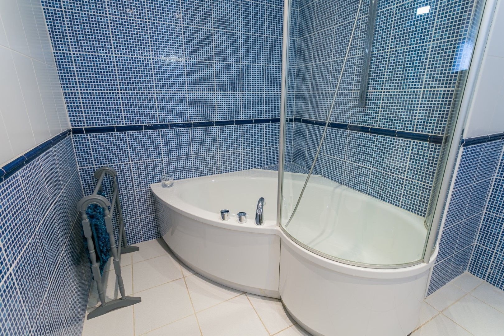 A corner bathroom with a white bathtub, a glass-enclosed shower, and blue mosaic tiles.