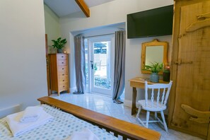 A bedroom with a bed, a wooden dresser, a desk with a chair, a mirror, and a television.