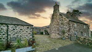 A stone building with a cobblestone courtyard, a staircase, and a small garden area with potted plants. - Tal y Bont Barns -  a remote that sleeps 24 guests  in 9 bedrooms (Bangor)