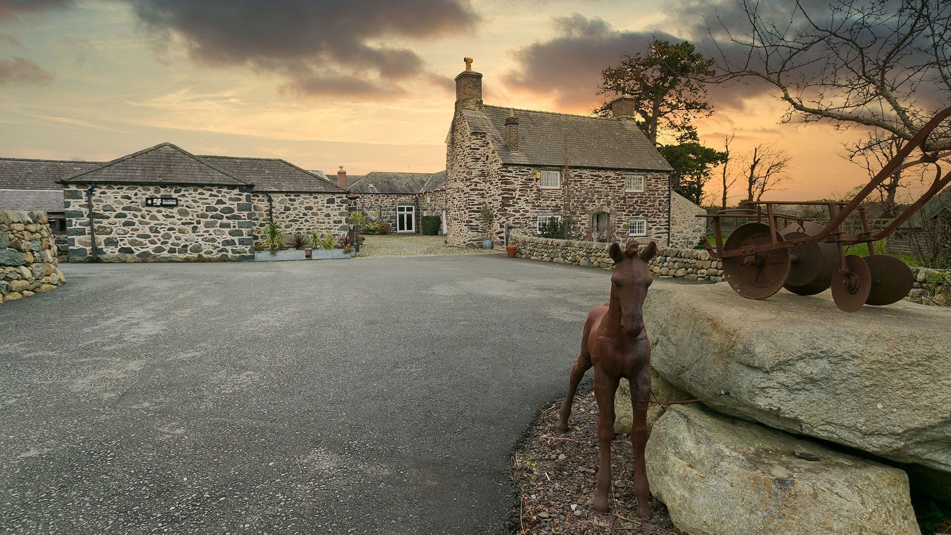 A stone building with a paved driveway and a horse statue.