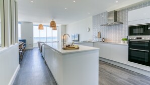 A modern kitchen with a central island, a built-in oven, and a view of the sea.