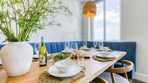 A dining area with a wooden table set for four, a vase of greenery, and a bottle of wine.