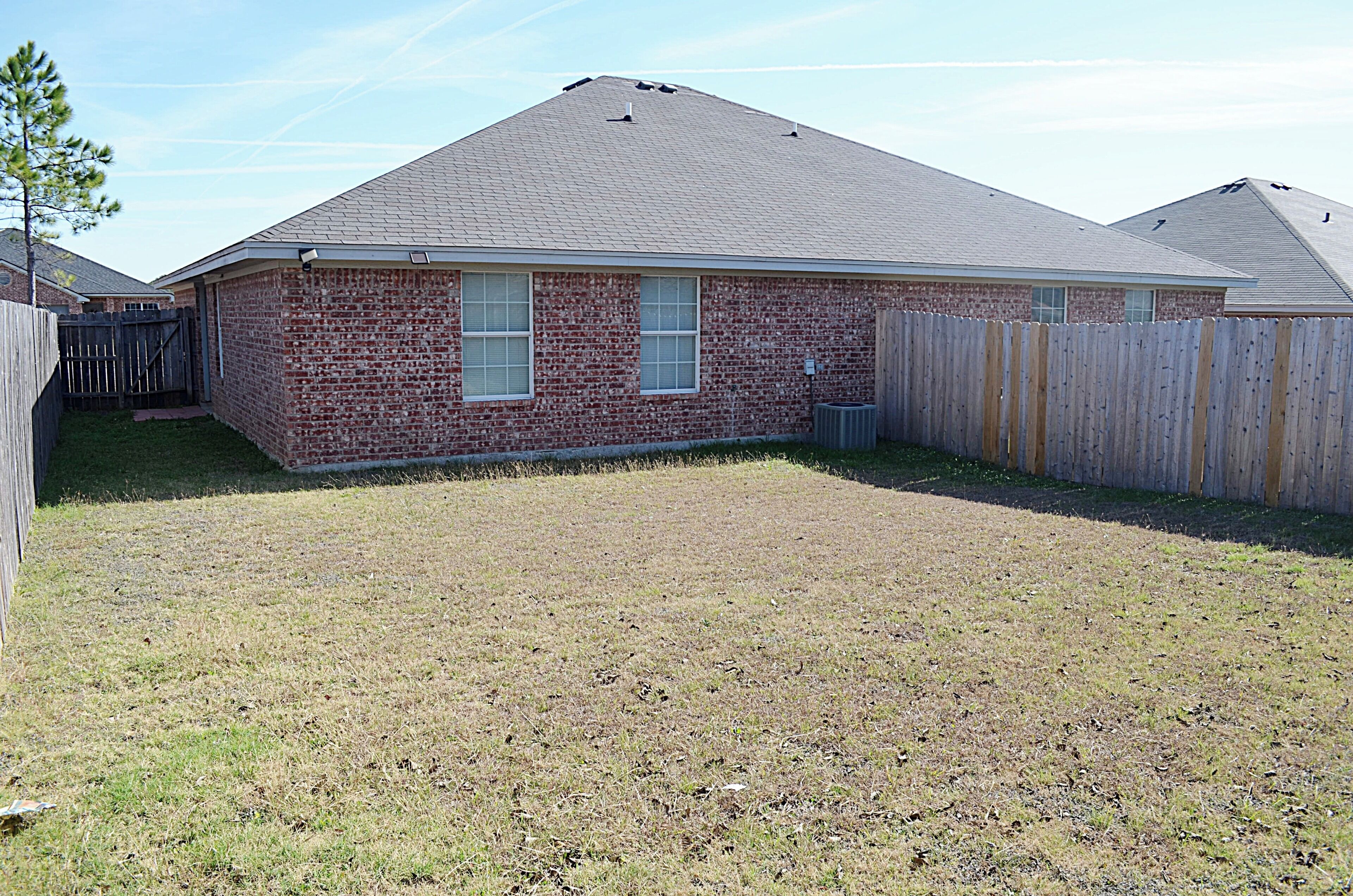 A single-story brick house with a sloped roof, a fenced backyard, and a visible chimney.