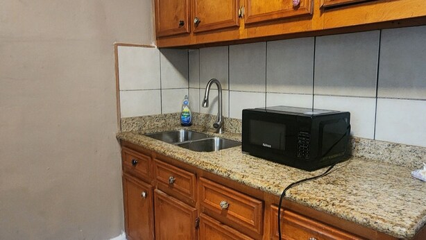 A kitchen with wooden cabinets, a granite countertop, a microwave, and a sink. - Bay Inn (Dickinson)