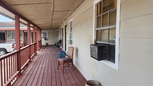 A covered porch with a wooden floor, a red railing, and a row of chairs. There are air conditioning units mounted on the wall. - Bay Inn (Dickinson)