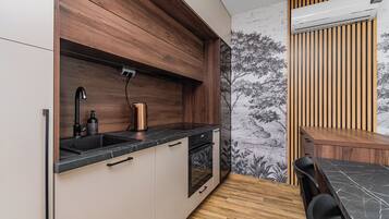 Een kleine keuken met een inbouwoven, een spoelbak en een houten spatwand.