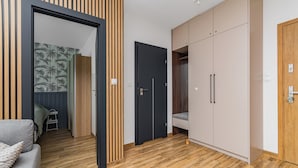 A modern room with a wooden floor, a grey sofa, a wardrobe, and a door leading to another room. - Perła Mierzei by Grand Apartments (Sztutowo)