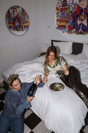 A room with a bed, a wall decoration, and a person pouring a drink.