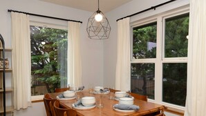 A dining room with a wooden table set for six, white curtains, and a geometric pendant light.