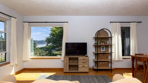A room with a large window, a TV on a wooden stand, a bookshelf, and a chair.
