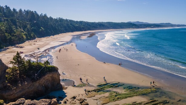 A coastal beach with clear skies, sandy shores, and rocky outcrops.