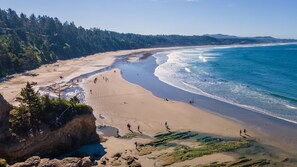 Una playa costera con cielos despejados, orillas de arena y afloramientos rocosos.