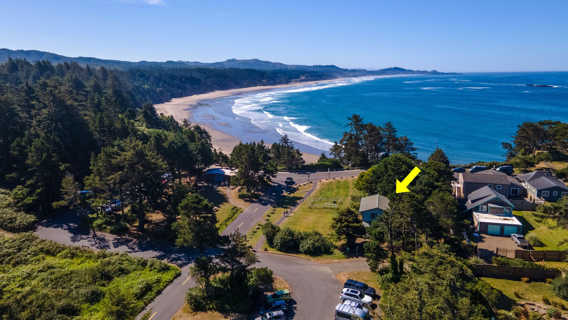 An aerial view of a coastal area with a beach, houses, and a road.