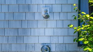 A building exterior with a shingled facade, a metal security camera, and a small window.