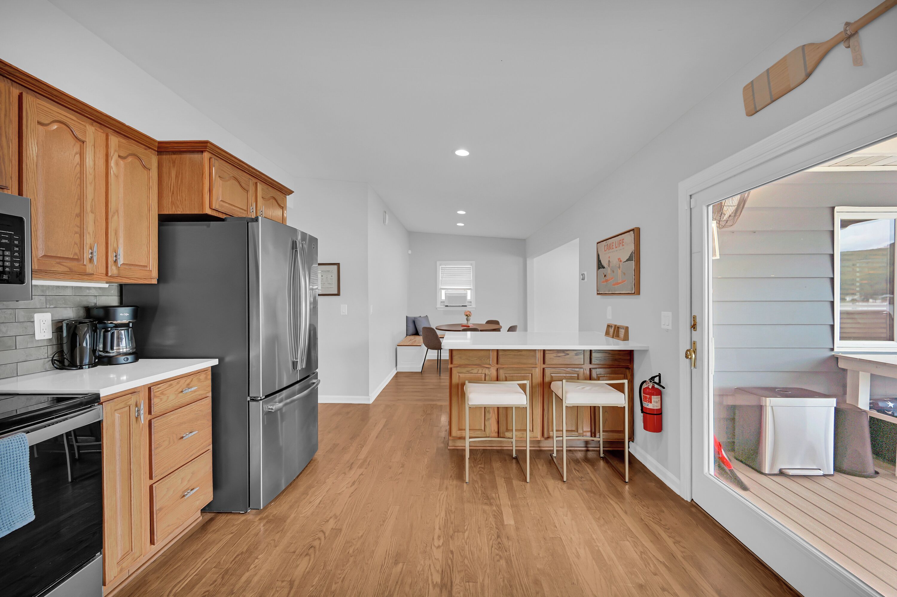 A modern kitchen with wooden cabinets, a stainless steel refrigerator, a built-in oven, and a bar area with stools.