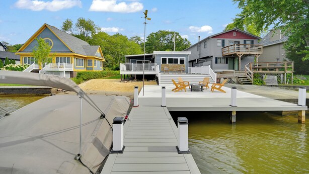 Un muelle con un bote, una casa con balcón y un pequeño edificio con mesas al aire libre.
