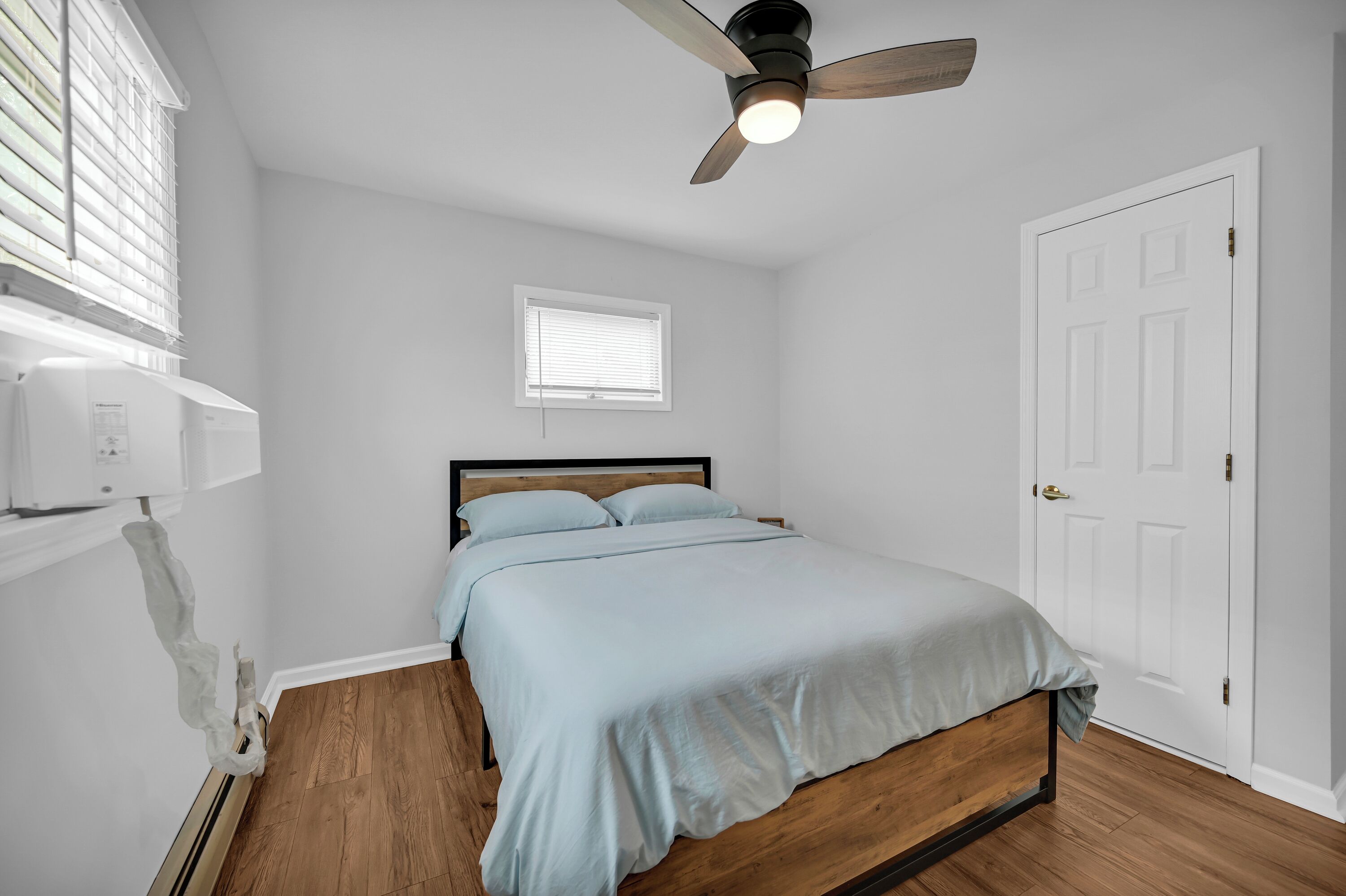 A bedroom with a bed, a ceiling fan, a window, and a door.