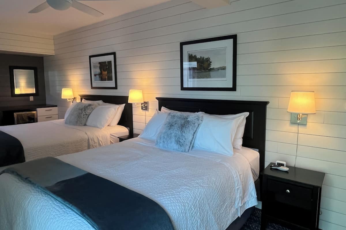 A hotel room with two beds, a ceiling fan, wall-mounted lamps, and framed pictures.