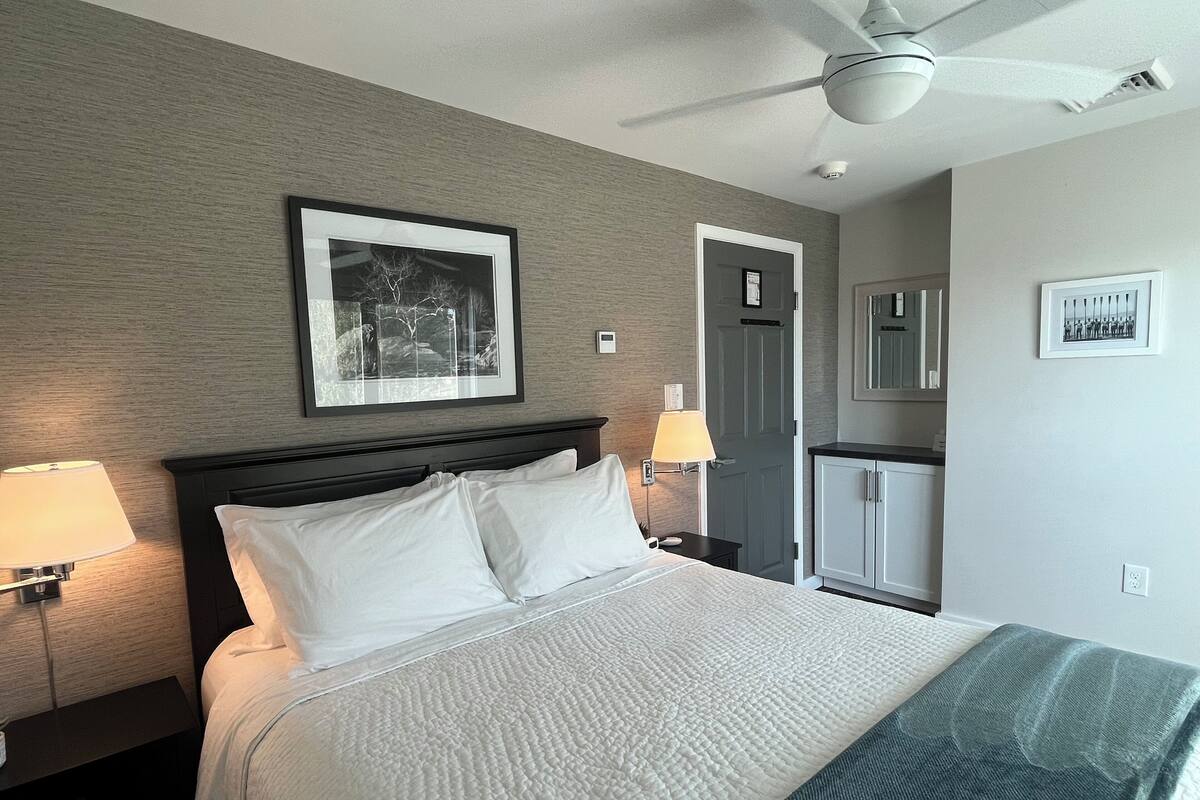 A neatly made bed with white linens, a headboard, and two bedside lamps.