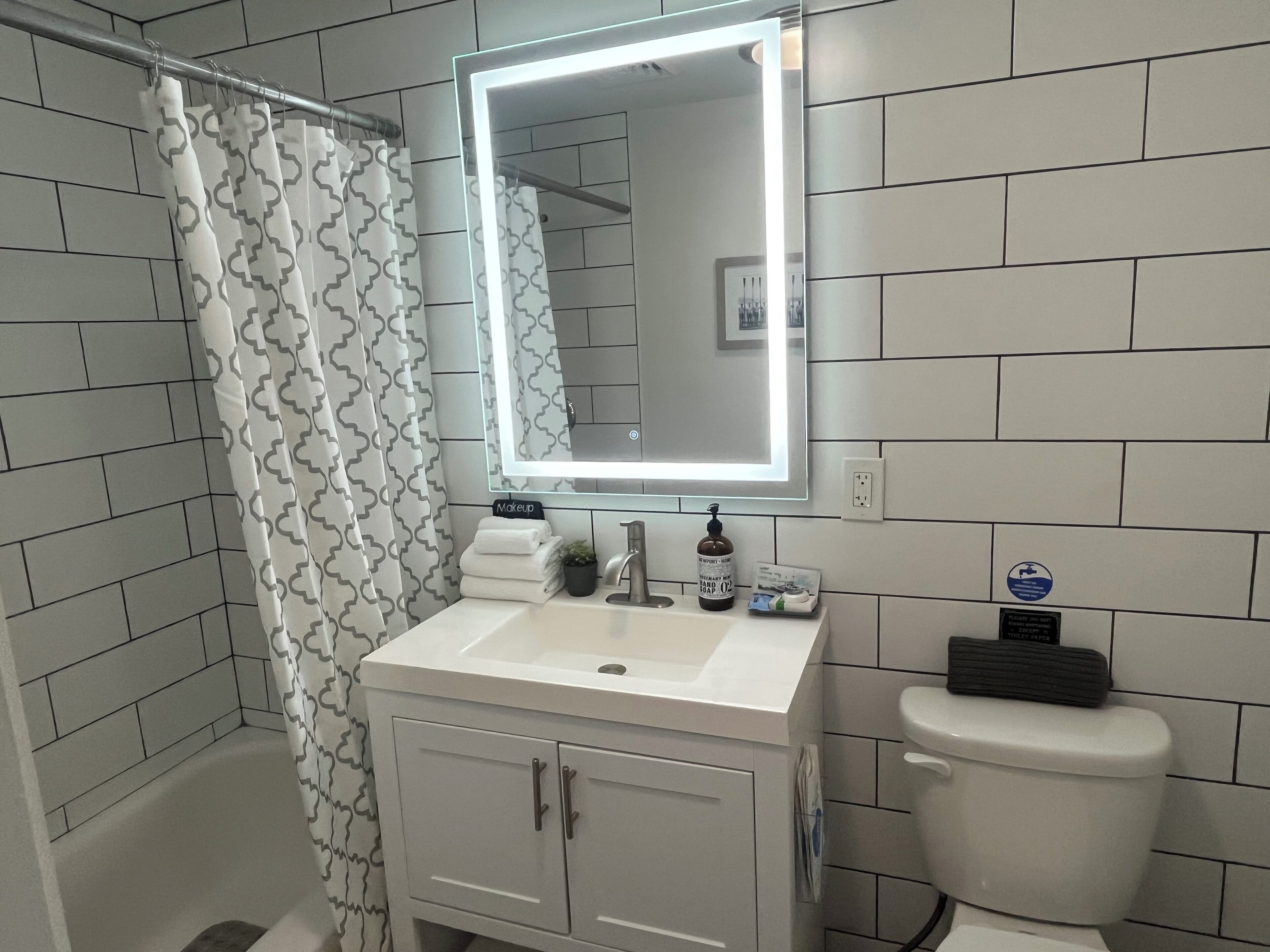 Un baño con lavamanos blanco, un espejo con luz, inodoro y cortina de ducha.