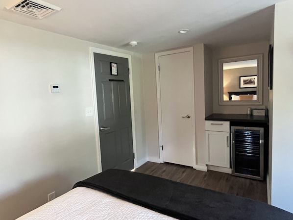 Un dormitorio con cama, armario, una pequeña kitchenette y una puerta que da a otra habitación.