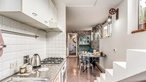 A modern kitchen with white cabinets, a gas stove, and a dining area with a table and chairs. - One Bedroom Apartment (ROMA)