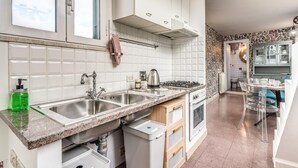 A modern kitchen with white cabinets, a double sink, a gas stove, and a dining area with clear chairs. - One Bedroom Apartment (ROMA)