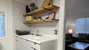 A compact kitchen with white subway tiles, wooden shelves, a built-in sink, and a small island with drawers.