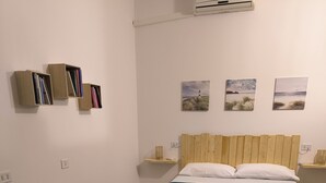 A room with a bed, two bedside tables, a bench, and a wall-mounted shelf with books. - Trinity House (Castellammare del Golfo)
