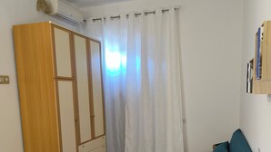 A room with a bed, a blue sofa, a wooden wardrobe, a patterned floor, and a window with curtains. - Trinity House (Castellammare del Golfo)