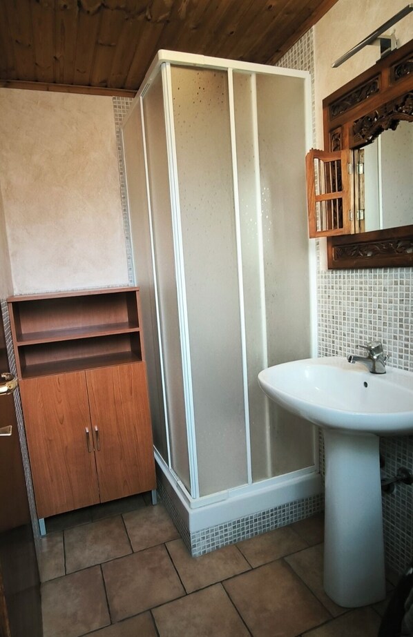 A bathroom with a shower enclosure, a wooden cabinet, a sink, and a tiled floor.