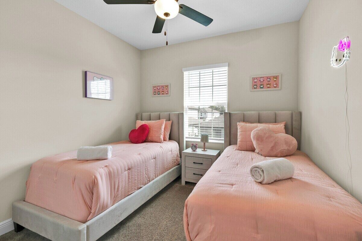 A bedroom with two beds, a ceiling fan, a window with blinds, and wall decorations.