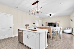 Una cocina moderna con una isla central, un comedor con mesa y sillas, y un ventilador de techo.