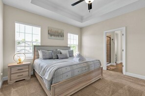 Une chambre à coucher comprenant un lit, des tables de chevet, un ventilateur de plafond et une porte donnant sur une autre pièce.