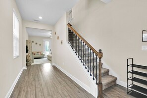 Una escalera con barandilla de madera y balaustradas negras, que conduce a un rellano con pared blanca y estante metálico negro.