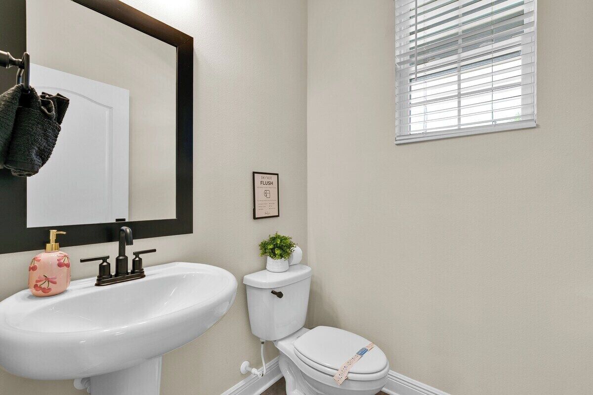 Un baño con lavamanos blanco, inodoro, espejo y ventana con persianas.
