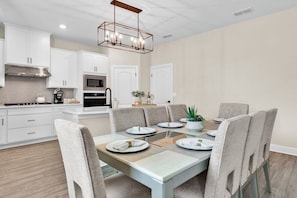 A modern kitchen with white cabinetry, a stainless steel range, and a dining area with a glass table and grey upholstered chairs.