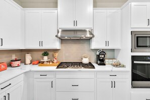 Une cuisine avec des meubles blancs, une cuisinière et un four à micro-ondes.