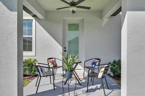 Un patio exterior con ventilador de techo, dos sillas, una mesa y una planta en maceta.