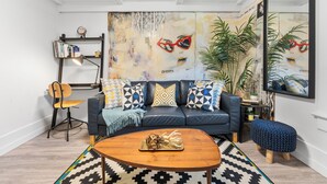 A modern living room with a dark blue sofa, patterned cushions, a wooden coffee table, and a large mirror.
