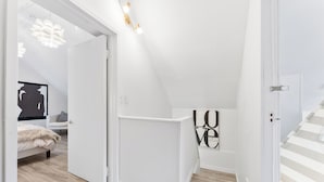 A modern, white-themed bedroom with a loft-style ceiling, a bed with a fur throw, and a large 'LOVE' sign on the wall.