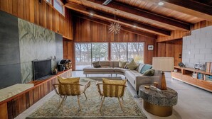 A modern living room with a sectional sofa, two armchairs, a coffee table, and a TV on a wooden wall. - Mid-Century Haven with Private Lakes and Endless Views (Erhard)