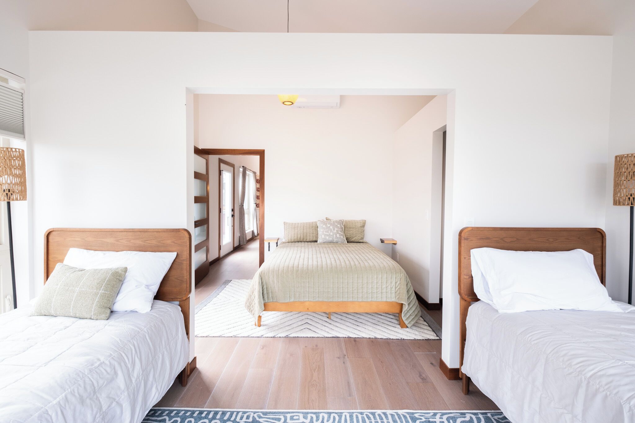 Une chambre d’hôtel avec deux lits, une tête de lit en bois, un tapis à motifs et un couloir menant à une autre pièce.