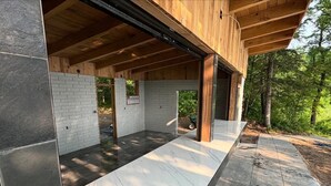 A modern building with a wooden exterior and a covered patio area with a marble floor. - Mid-Century Haven with Private Lakes and Endless Views (Erhard)